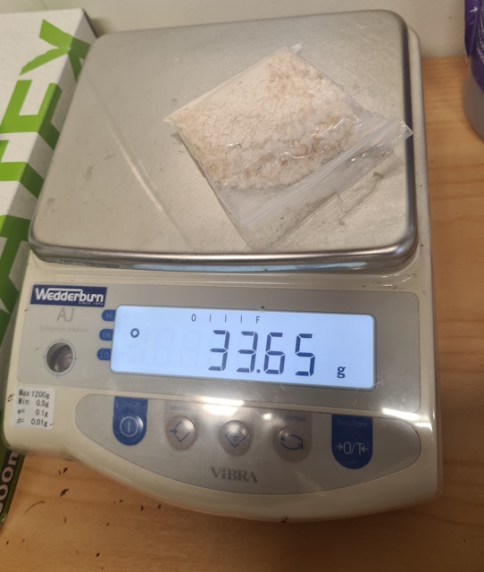 A packet of white substance being weighed on a scale. The scale reads 33.65 grams.